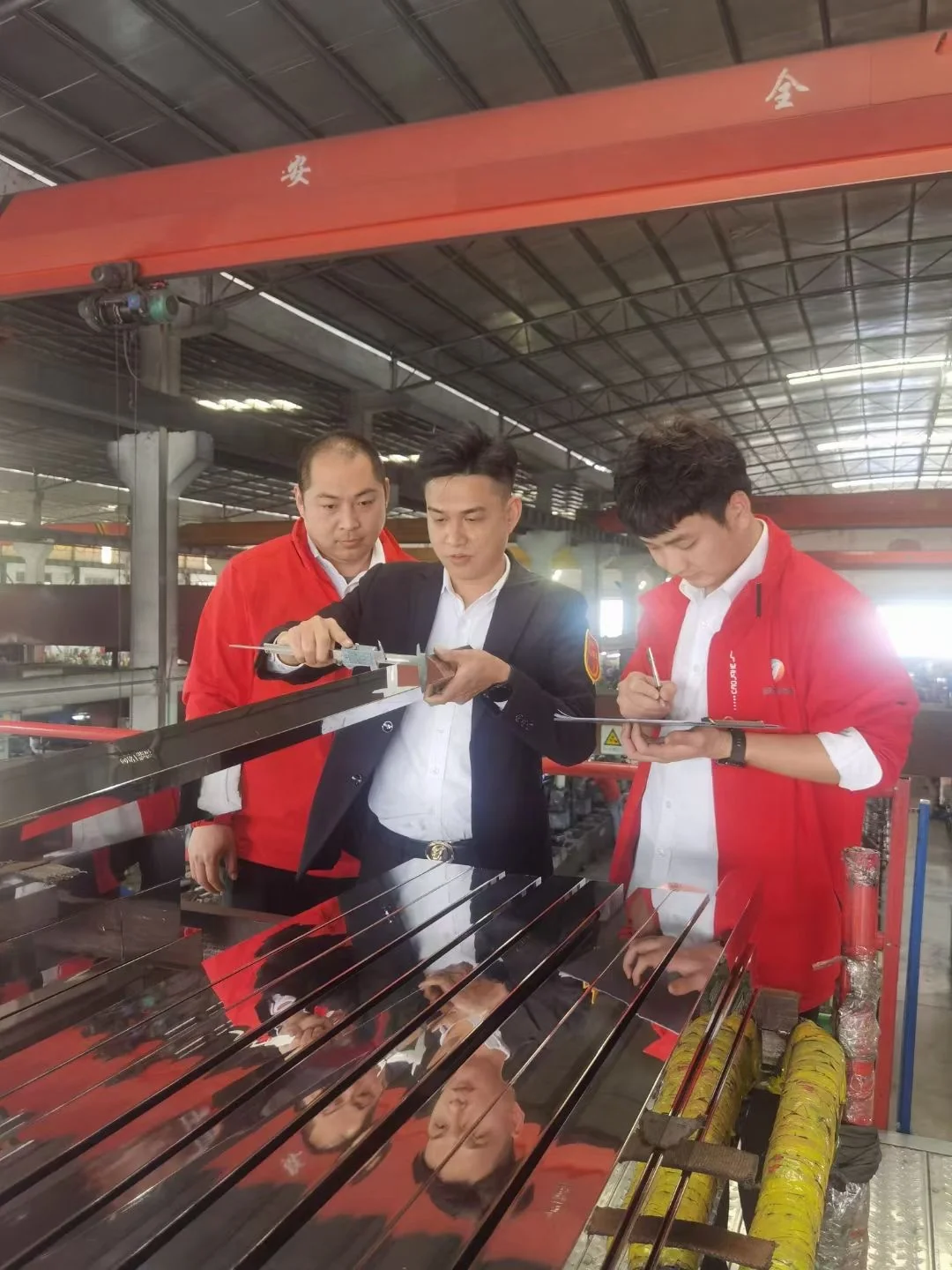 Factory team measuring and recording stainless steel tube dimensions during quality inspection
